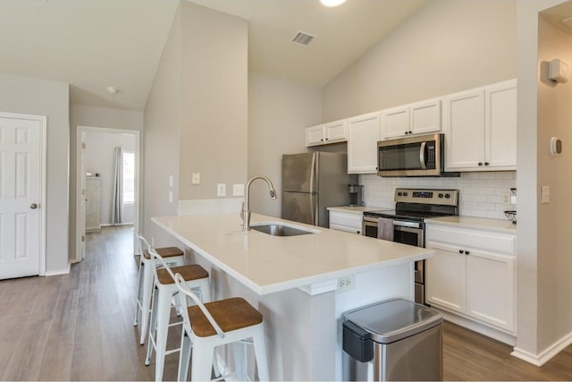 kitchen with decorative backsplash, appliances with stainless steel finishes, hardwood / wood-style flooring, sink, and lofted ceiling