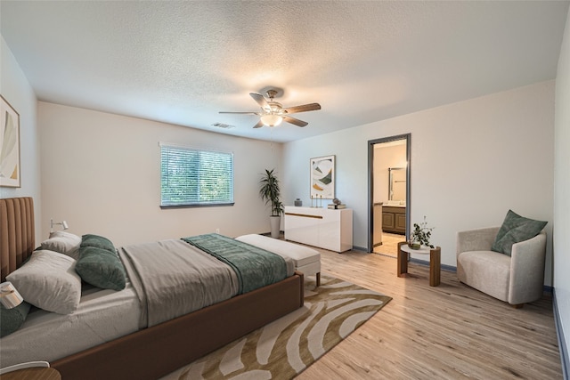 bedroom featuring ceiling fan, light wood-type flooring, a textured ceiling, and ensuite bath