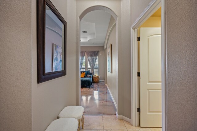 hall featuring a tray ceiling and light tile patterned floors