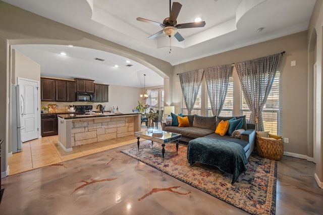 living room featuring ceiling fan with notable chandelier, a raised ceiling, light tile patterned floors, and sink