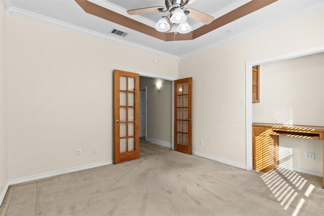 empty room with ornamental molding, french doors, a raised ceiling, light colored carpet, and ceiling fan