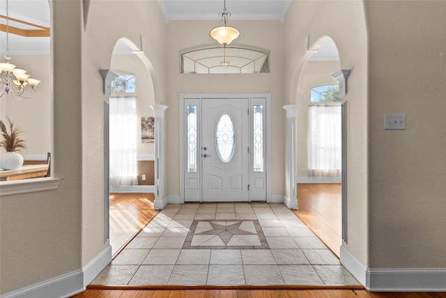 tiled foyer entrance with crown molding and a chandelier