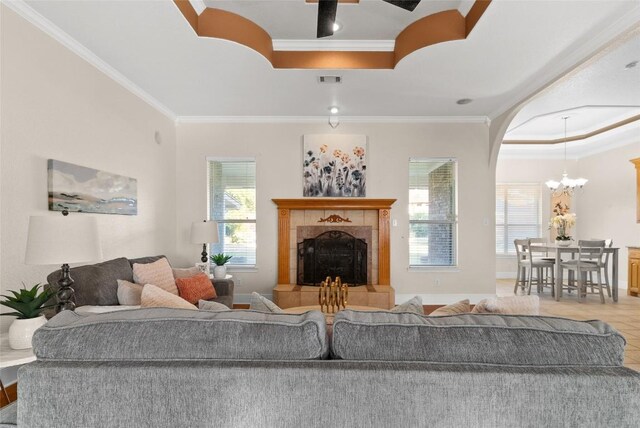 tiled living room featuring a fireplace, a notable chandelier, ornamental molding, and a tray ceiling