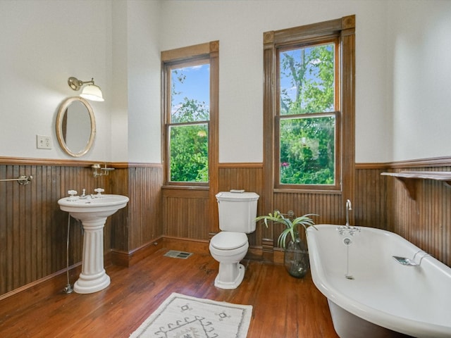 bathroom featuring a bath, wooden walls, a healthy amount of sunlight, and toilet