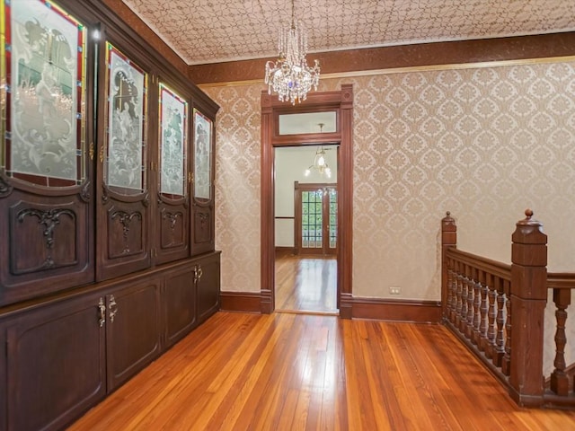 foyer with crown molding, light wood-style flooring, a notable chandelier, and wallpapered walls