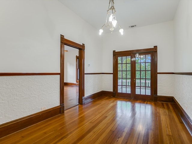 spare room featuring a notable chandelier, french doors, and wood-type flooring