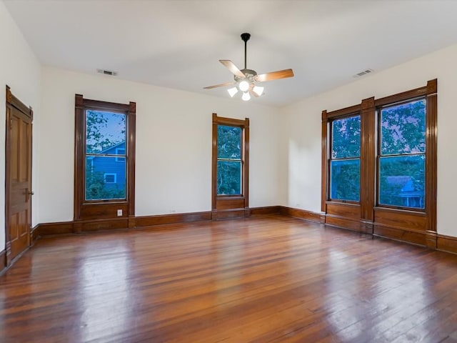 spare room featuring a healthy amount of sunlight, visible vents, baseboards, and wood finished floors