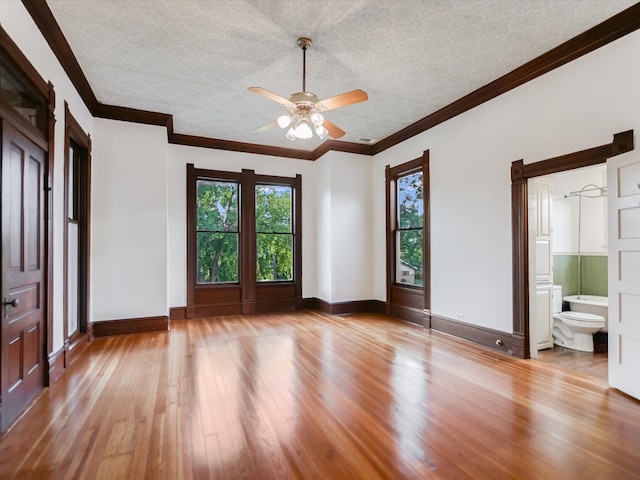 unfurnished bedroom featuring ceiling fan, hardwood / wood-style floors, ornamental molding, ensuite bath, and a textured ceiling