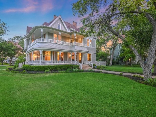 back of property at dusk with a porch, a chimney, a lawn, and a balcony