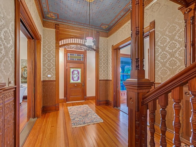 entrance foyer with light wood finished floors, ornamental molding, wallpapered walls, and a wainscoted wall
