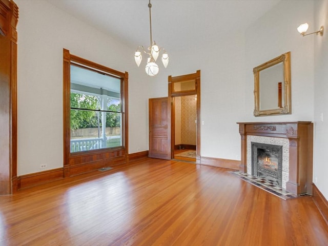 unfurnished living room with visible vents, baseboards, a chandelier, a fireplace, and wood finished floors