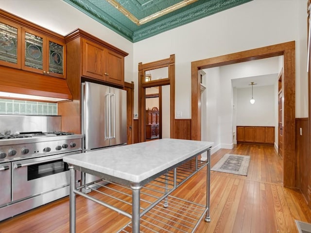 kitchen with wainscoting, light wood-style floors, brown cabinetry, and high quality appliances