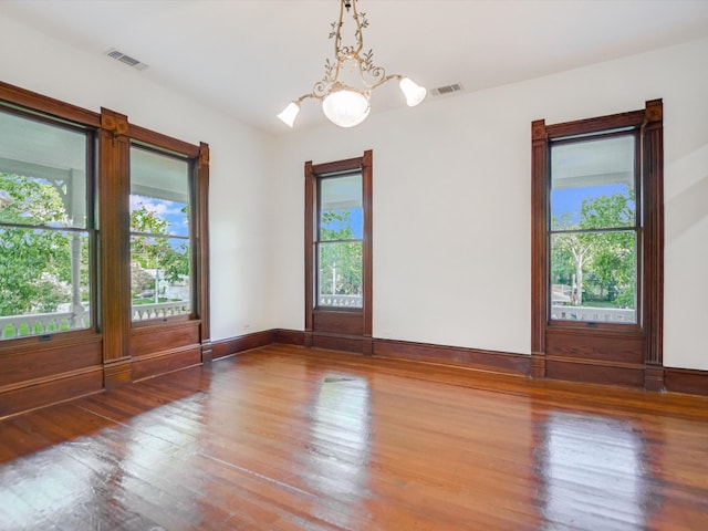 unfurnished room with a wealth of natural light, a notable chandelier, and wood-type flooring