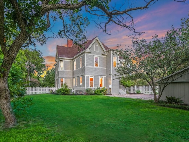 back of house at dusk featuring a yard, fence, and a chimney