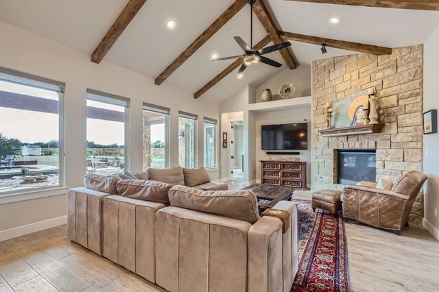 living room with ceiling fan, light wood-type flooring, a stone fireplace, high vaulted ceiling, and beam ceiling