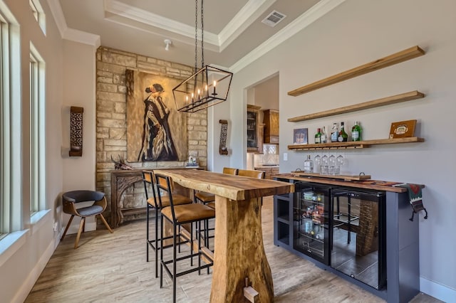 dining space with light hardwood / wood-style flooring, a tray ceiling, a wealth of natural light, crown molding, and bar area