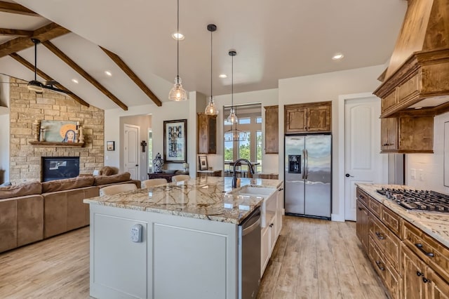 kitchen with a large island with sink, beam ceiling, light hardwood / wood-style floors, a fireplace, and stainless steel appliances