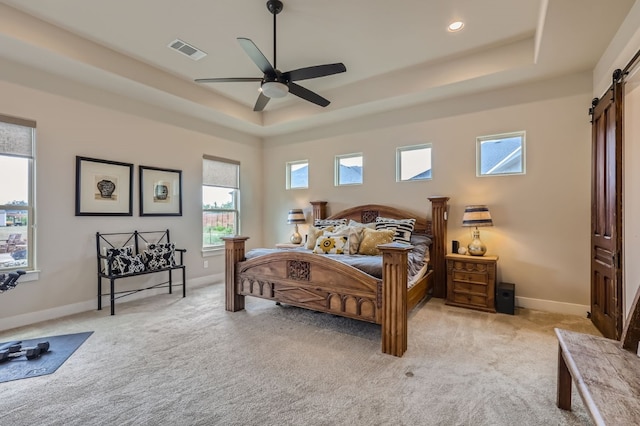 carpeted bedroom with ceiling fan, a raised ceiling, and a barn door