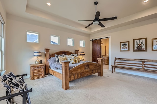 carpeted bedroom with ceiling fan, a raised ceiling, a barn door, and multiple windows