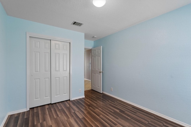 unfurnished bedroom with a closet, a textured ceiling, and dark hardwood / wood-style floors