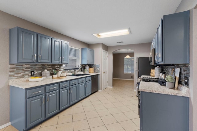 kitchen with stainless steel appliances, tasteful backsplash, sink, light stone counters, and light tile patterned floors