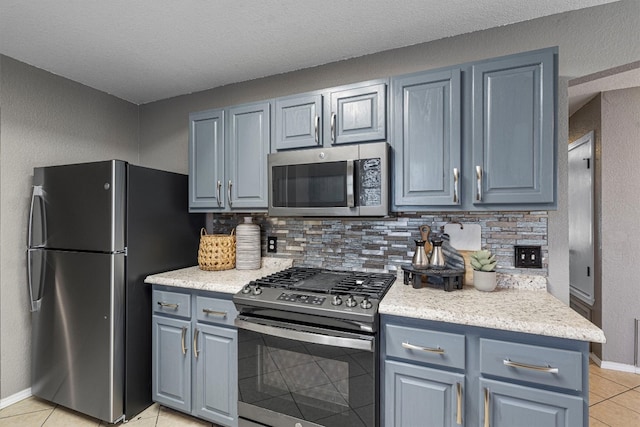 kitchen featuring light tile patterned floors, stainless steel appliances, decorative backsplash, and a textured ceiling