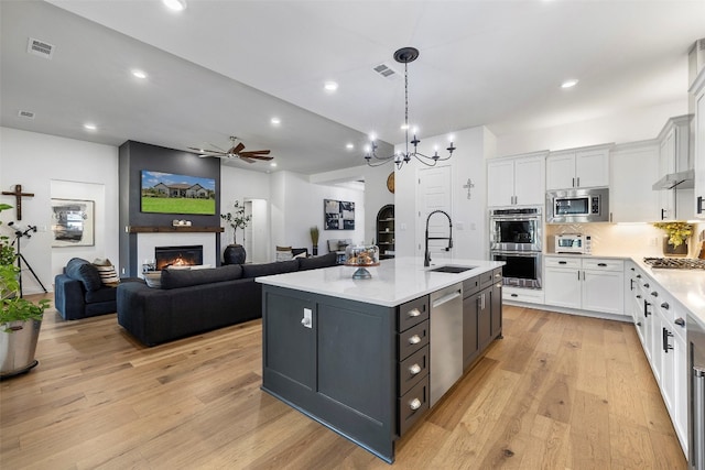 kitchen featuring white cabinets, light hardwood / wood-style flooring, a center island with sink, and stainless steel appliances