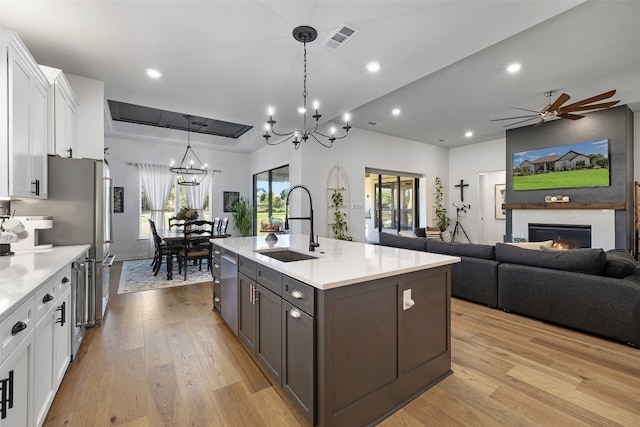 kitchen featuring white cabinetry, light hardwood / wood-style flooring, ceiling fan with notable chandelier, and an island with sink