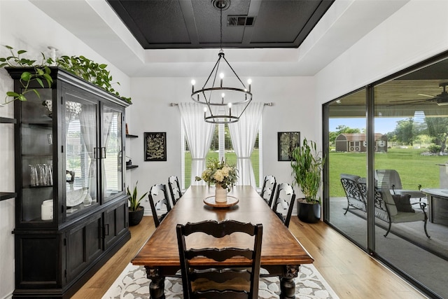 dining area with ceiling fan with notable chandelier, light hardwood / wood-style floors, and a tray ceiling