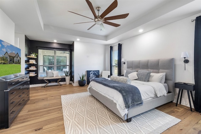 bedroom with ceiling fan, light hardwood / wood-style flooring, and a tray ceiling