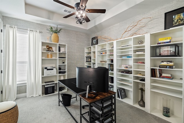 home office featuring a tray ceiling, carpet flooring, and ceiling fan