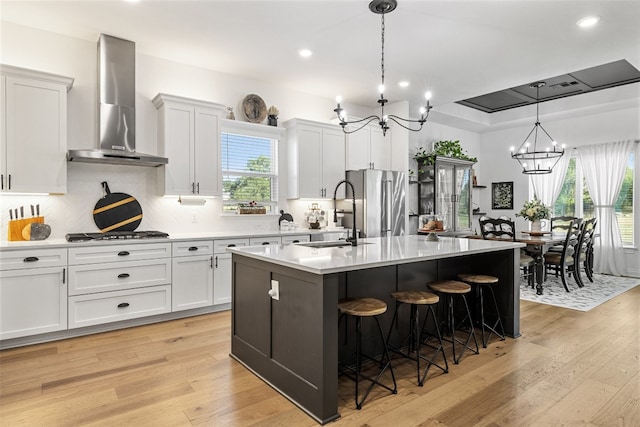 kitchen featuring hanging light fixtures, wall chimney exhaust hood, an island with sink, light hardwood / wood-style floors, and stainless steel appliances