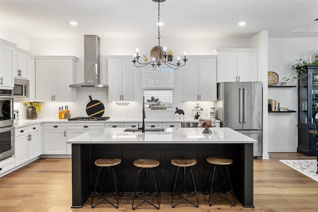 kitchen with stainless steel appliances, light hardwood / wood-style floors, an island with sink, and wall chimney exhaust hood