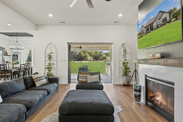 living room featuring a fireplace, ceiling fan with notable chandelier, and light wood-type flooring