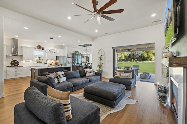 living room featuring sink, light wood-type flooring, and ceiling fan with notable chandelier