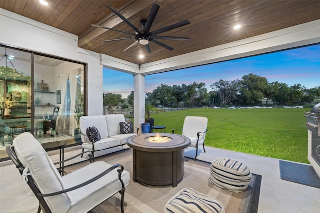 patio terrace at dusk with ceiling fan, an outdoor living space with a fire pit, and a lawn