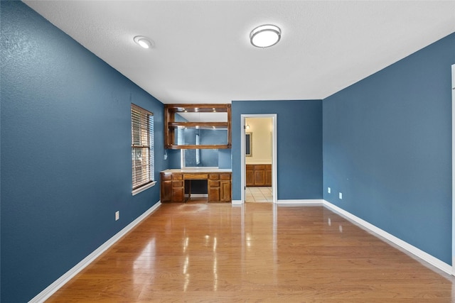 unfurnished living room with built in desk and light wood-type flooring