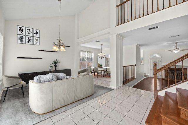 tiled living room with ceiling fan with notable chandelier, high vaulted ceiling, and decorative columns