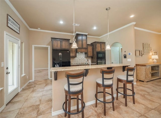 kitchen featuring pendant lighting, a breakfast bar area, black appliances, dark brown cabinets, and a center island with sink