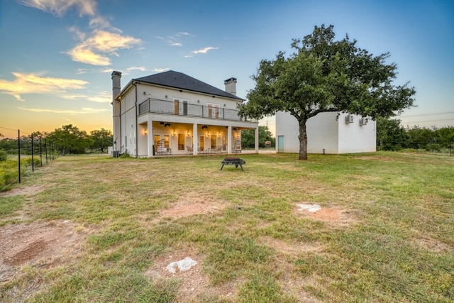 back house at dusk featuring a balcony and a yard