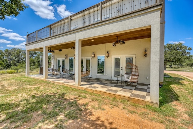 rear view of property with ceiling fan, a balcony, a patio area, a yard, and french doors