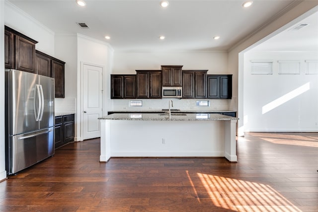 kitchen with backsplash, appliances with stainless steel finishes, dark wood-type flooring, light stone counters, and a center island with sink