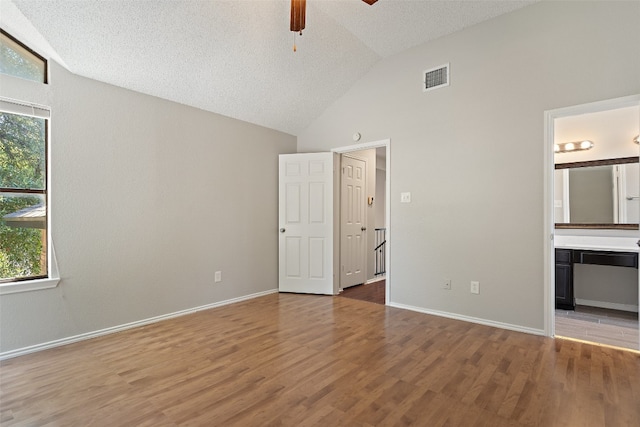 unfurnished bedroom featuring high vaulted ceiling, ensuite bath, a textured ceiling, ceiling fan, and hardwood / wood-style flooring