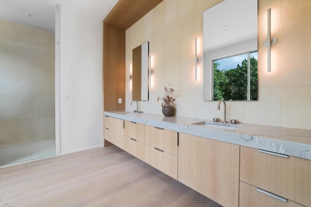 full bathroom with double vanity, tiled shower, wood finished floors, and a sink