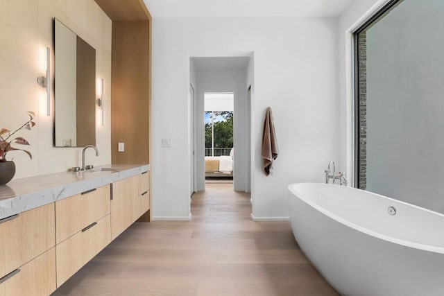 ensuite bathroom featuring vanity, wood finished floors, baseboards, ensuite bath, and a soaking tub