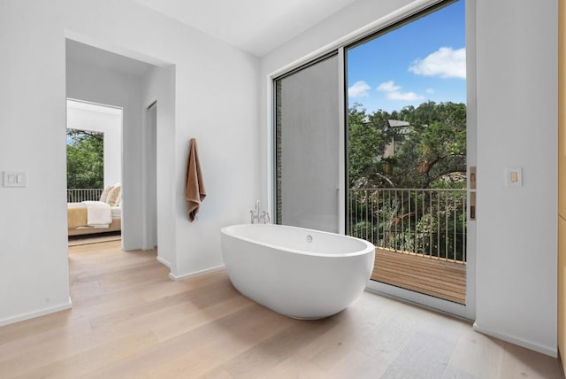 bathroom featuring a freestanding tub, wood finished floors, baseboards, and connected bathroom