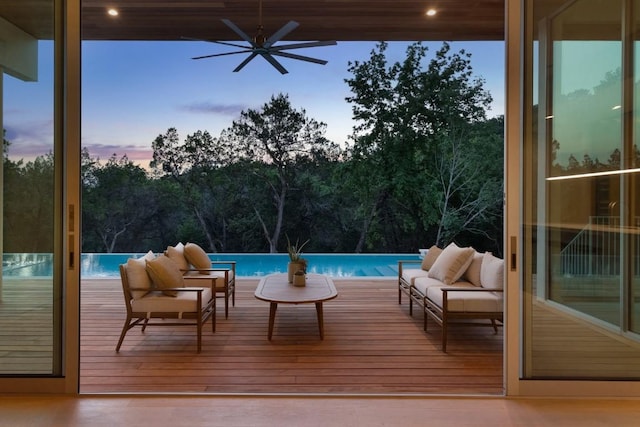 pool at dusk with an outdoor hangout area, a wooden deck, an infinity pool, and ceiling fan