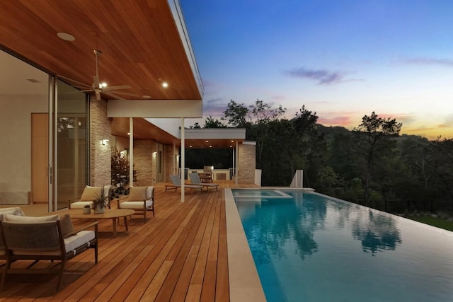 pool at dusk with an outdoor hangout area, an infinity pool, and a deck