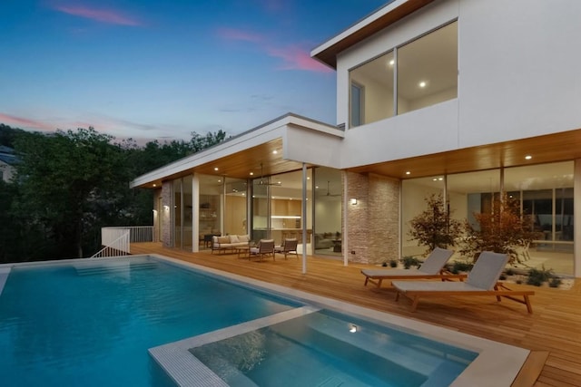 back of house at dusk with a deck, a balcony, and a pool with connected hot tub