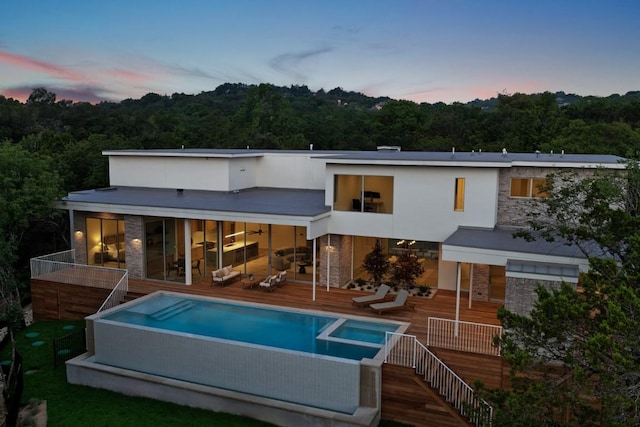 rear view of property featuring stairway, stone siding, a deck, and a pool with connected hot tub